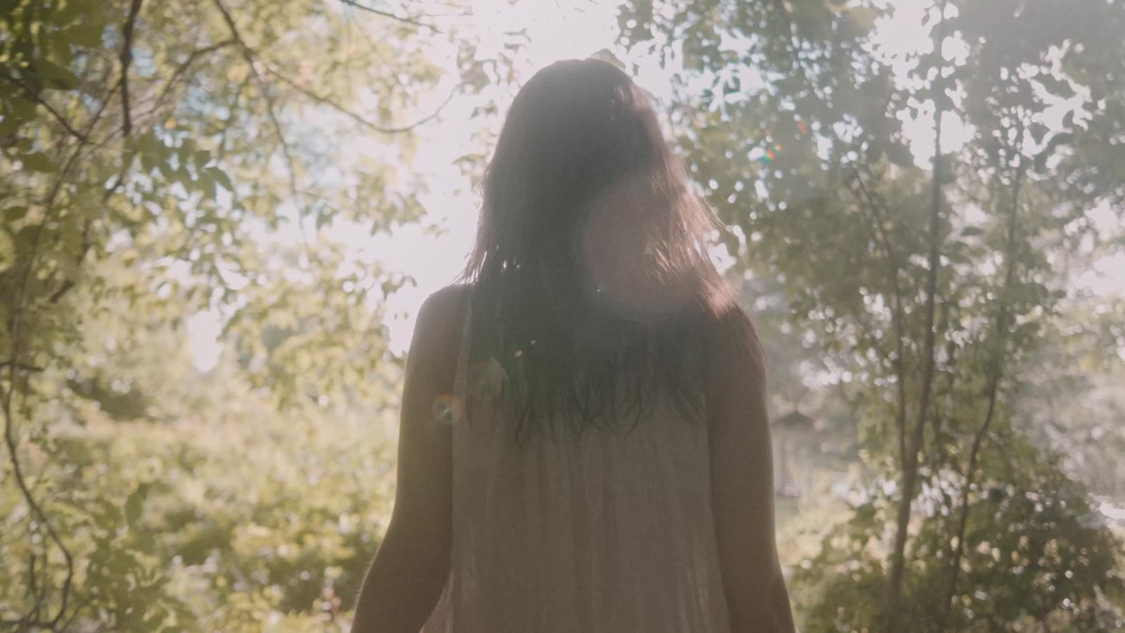 Woman in white walking into a sunlit forest